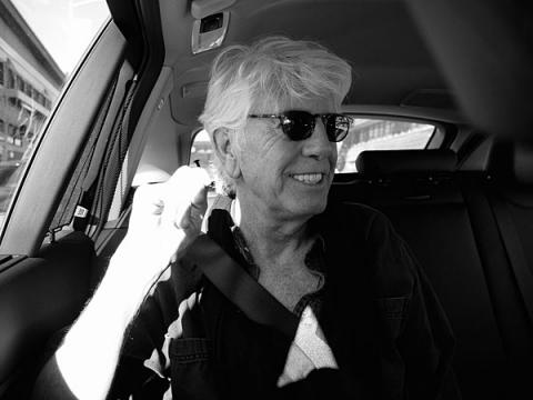 Graham Nash smiles in a car wearing black sunglasses