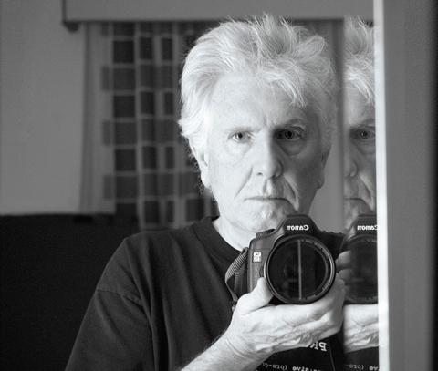 Graham Nash taking a photo of himself in the mirror. His face is serious and his grey white hair is swept back like had just ran his hand through it